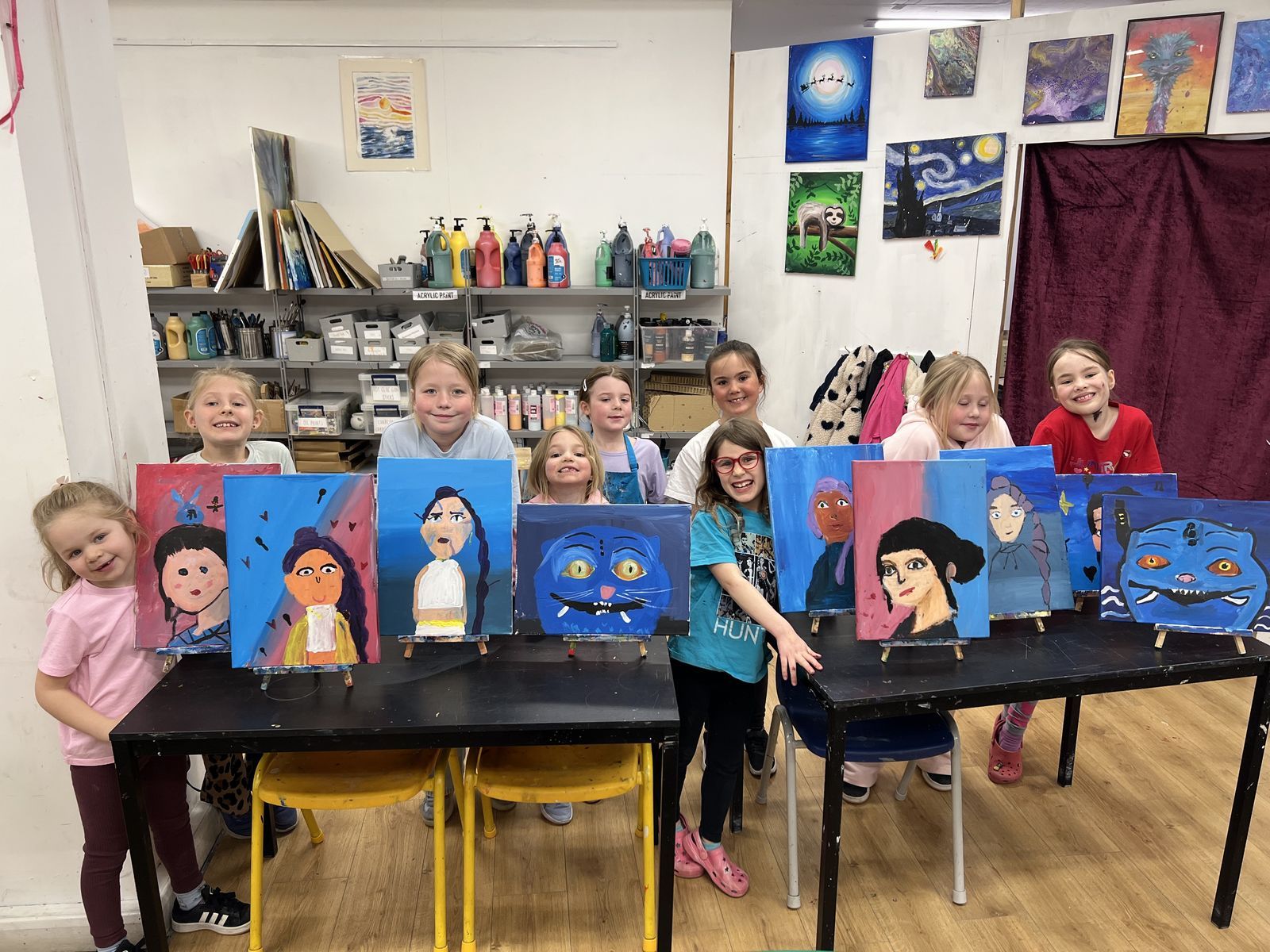 Children in the studio during the Easter holidays, standing behind a row of their bold, colourful portrait paintings