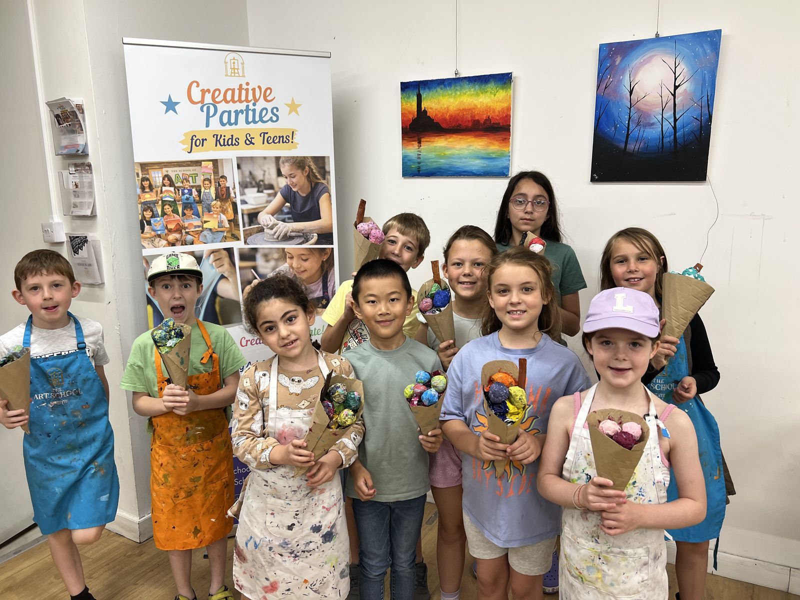 A group of smiling children in aprons holding the flower bouquets they made at a party