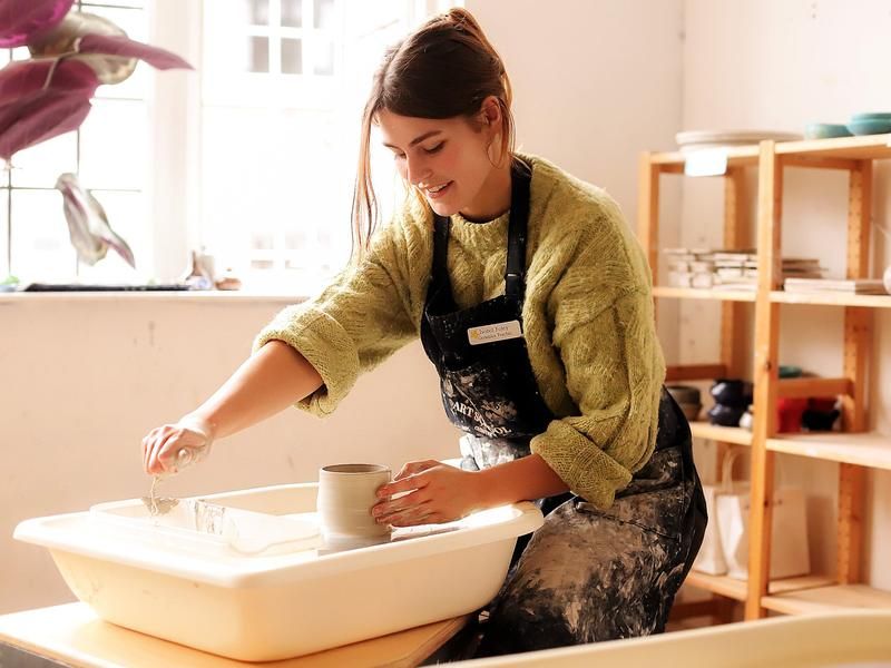 An adult student shaping clay on the pottery wheel