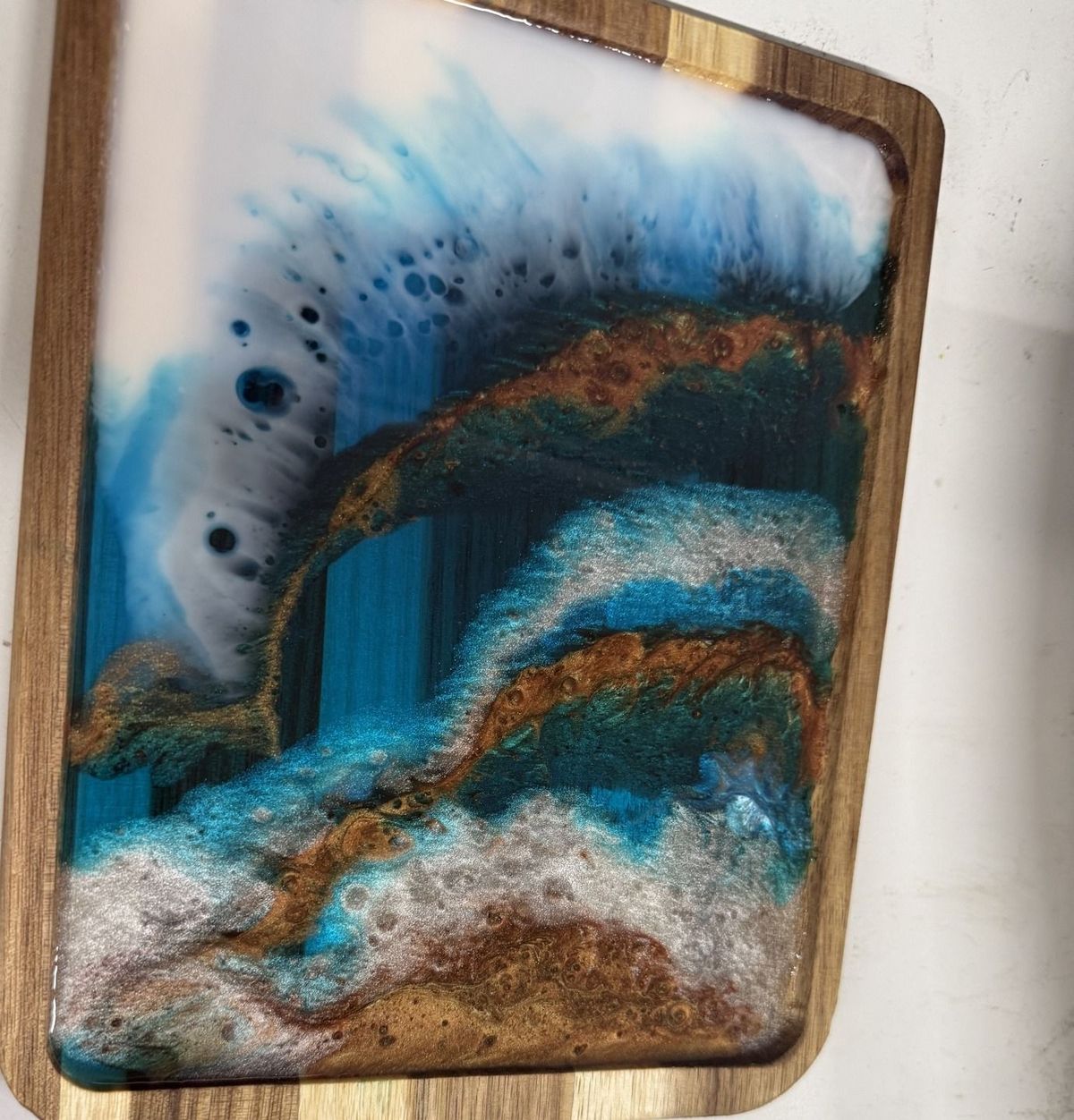 A resin serving board poured with ocean-wave blues and gold leaf